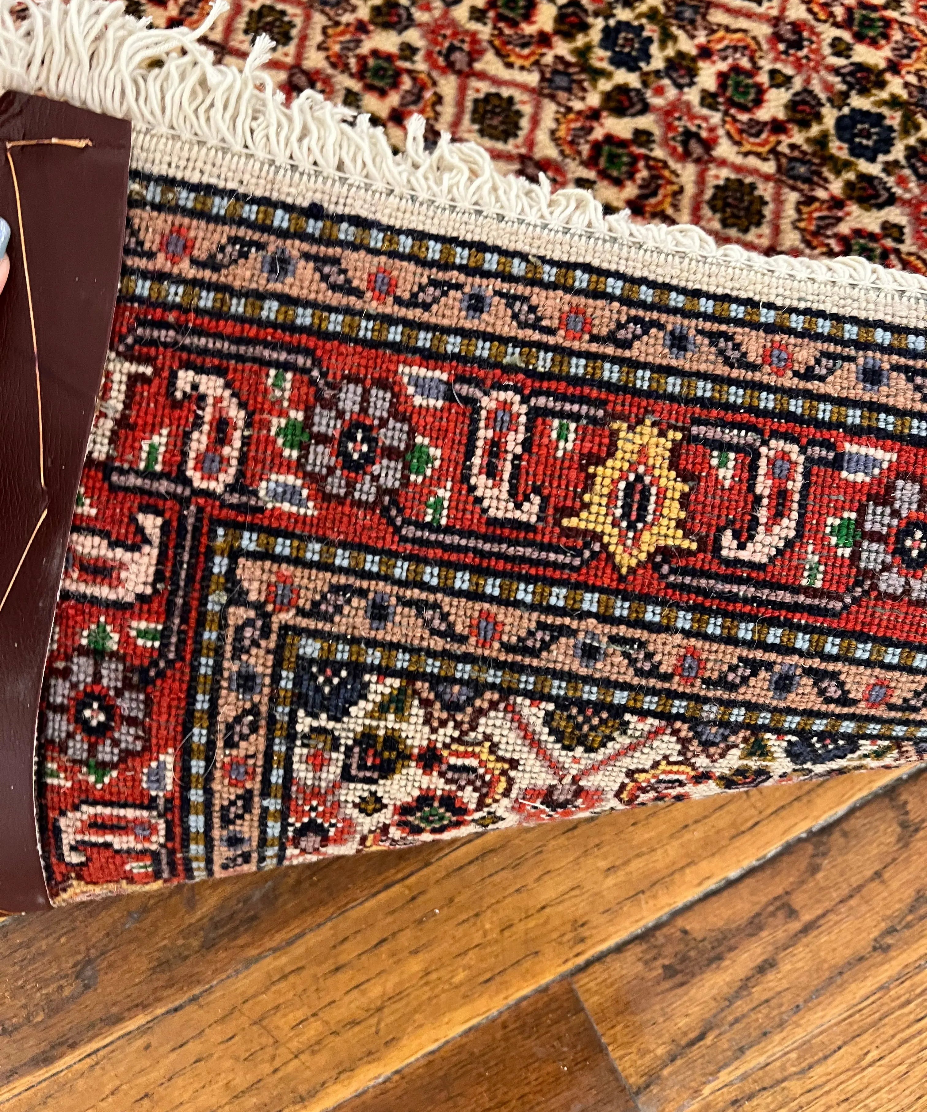 Persian-style rug corner with red, navy, and cream geometric bands and cream fringe