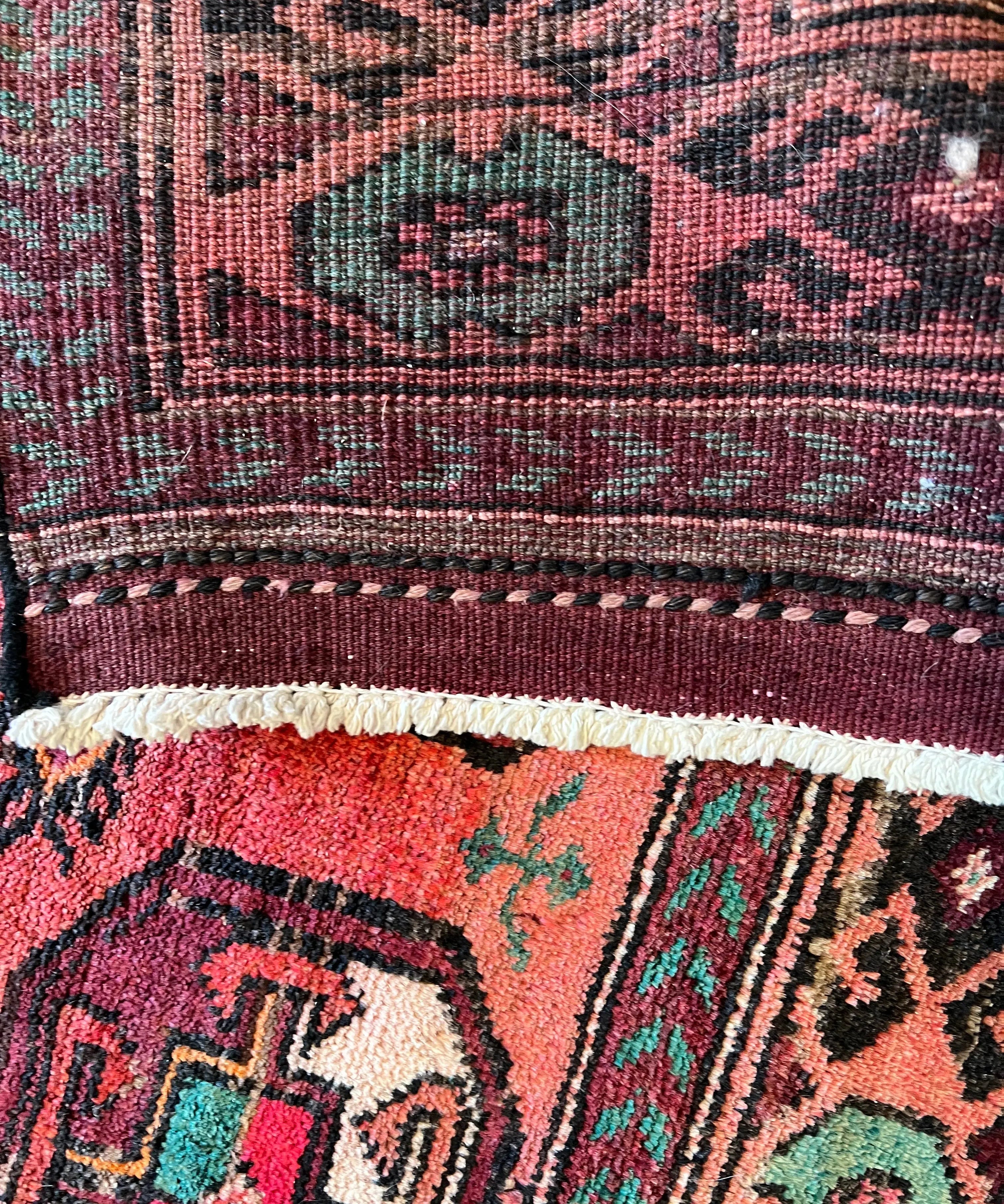 Red Persian tribal rug close-up with fringe edge and teal geometric motifs