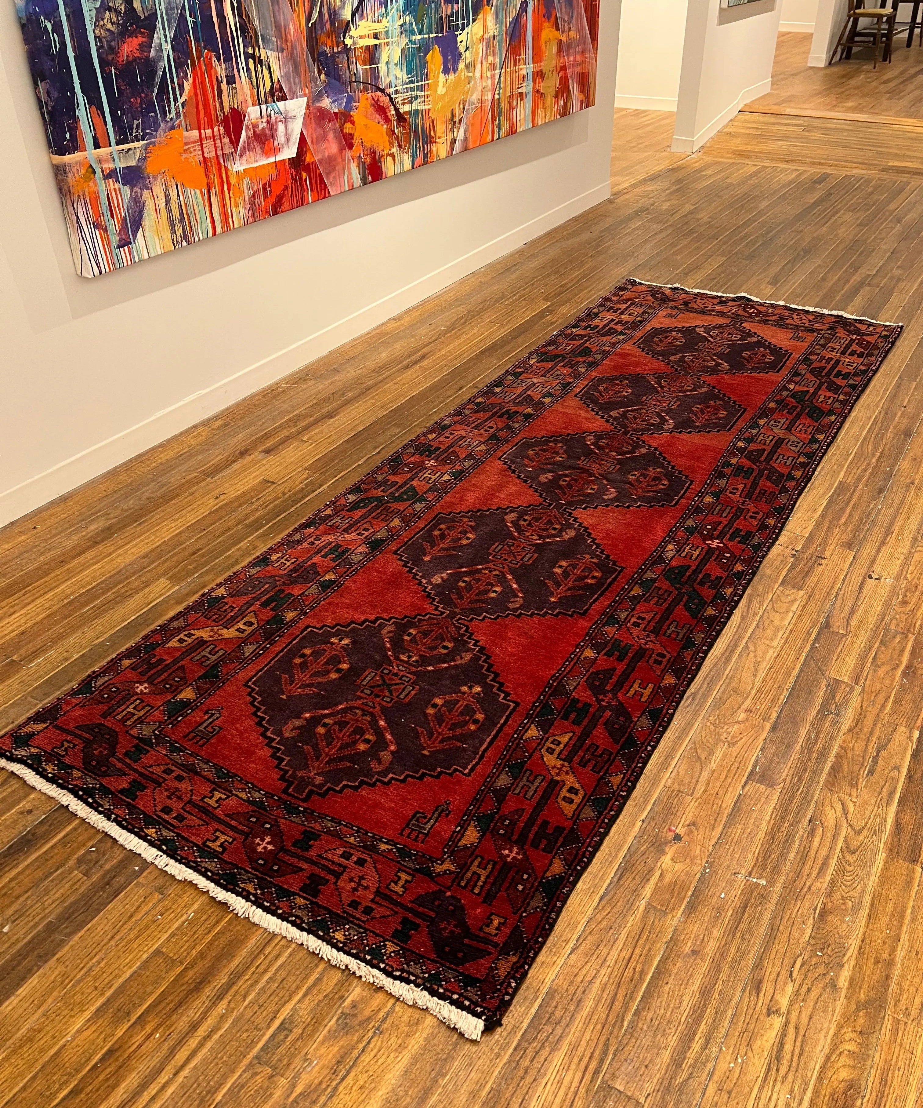 Vintage Persian-style runner rug on hardwood floor, red with geometric navy patterns and cream border