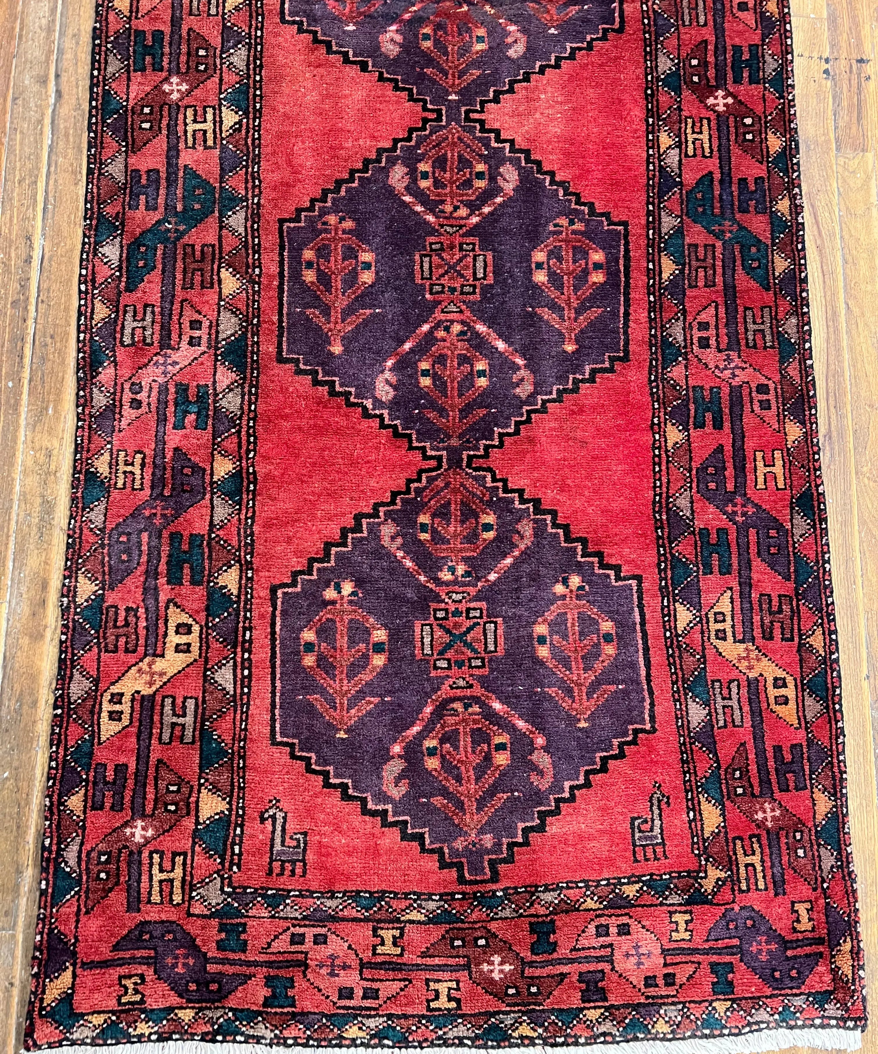 Vintage Persian-style runner rug close-up, red center with navy diamond motifs and cream fringe