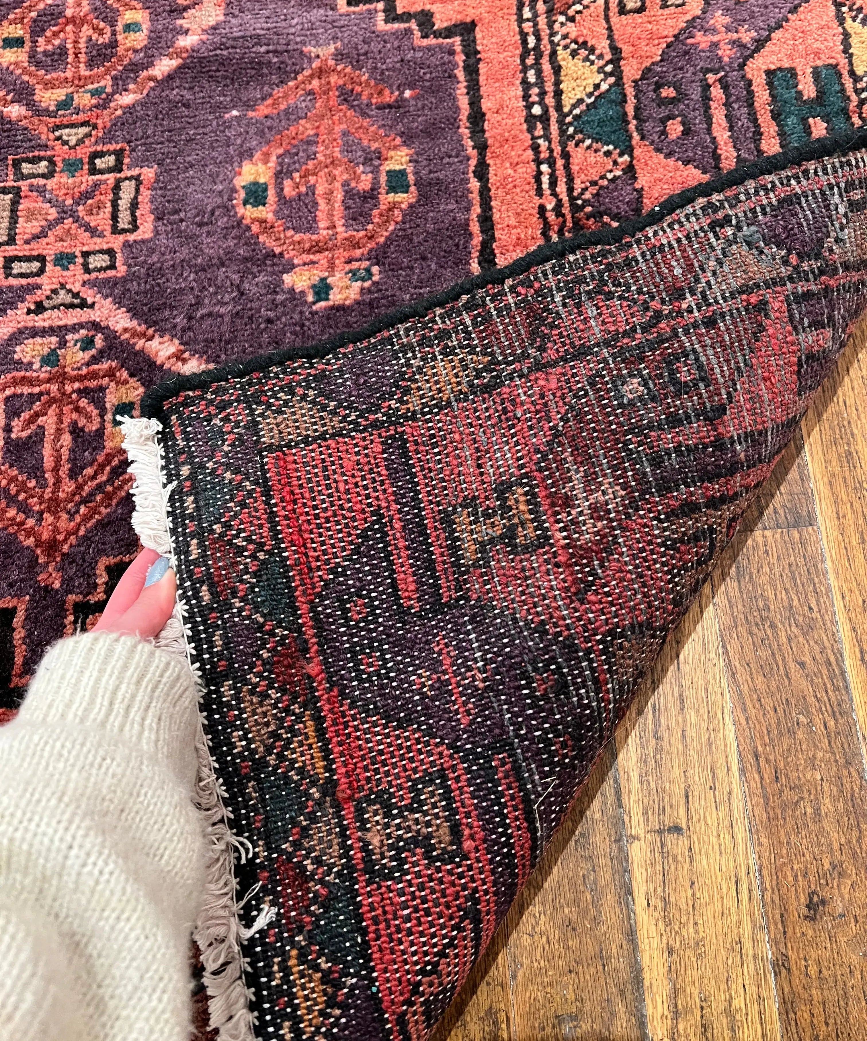 Vintage Persian-style runner rug corner close-up, red and navy weave with cream fringe edge