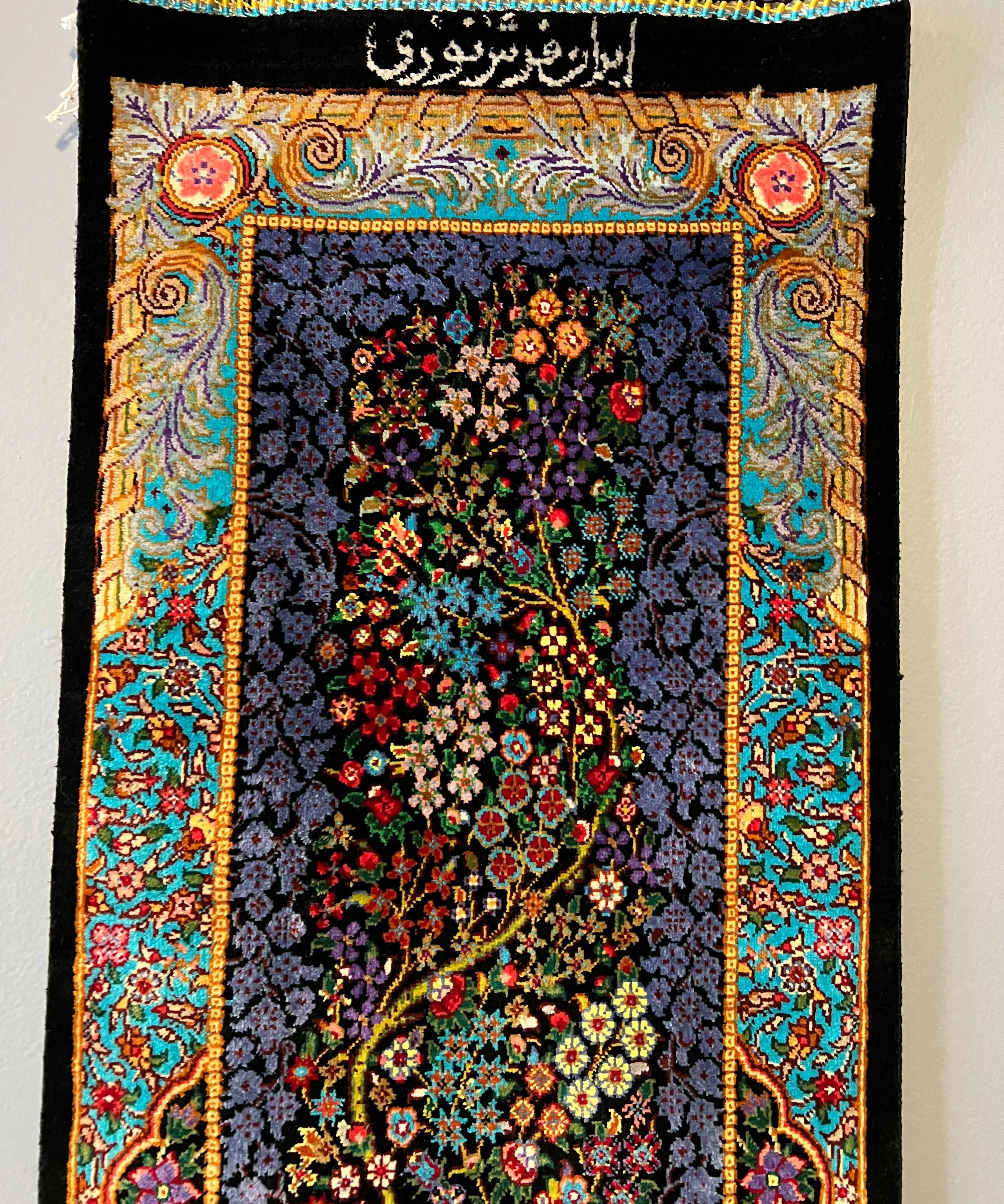 Silk tableau rug with beaded fringe and black top band of script, colorful floral centerpiece