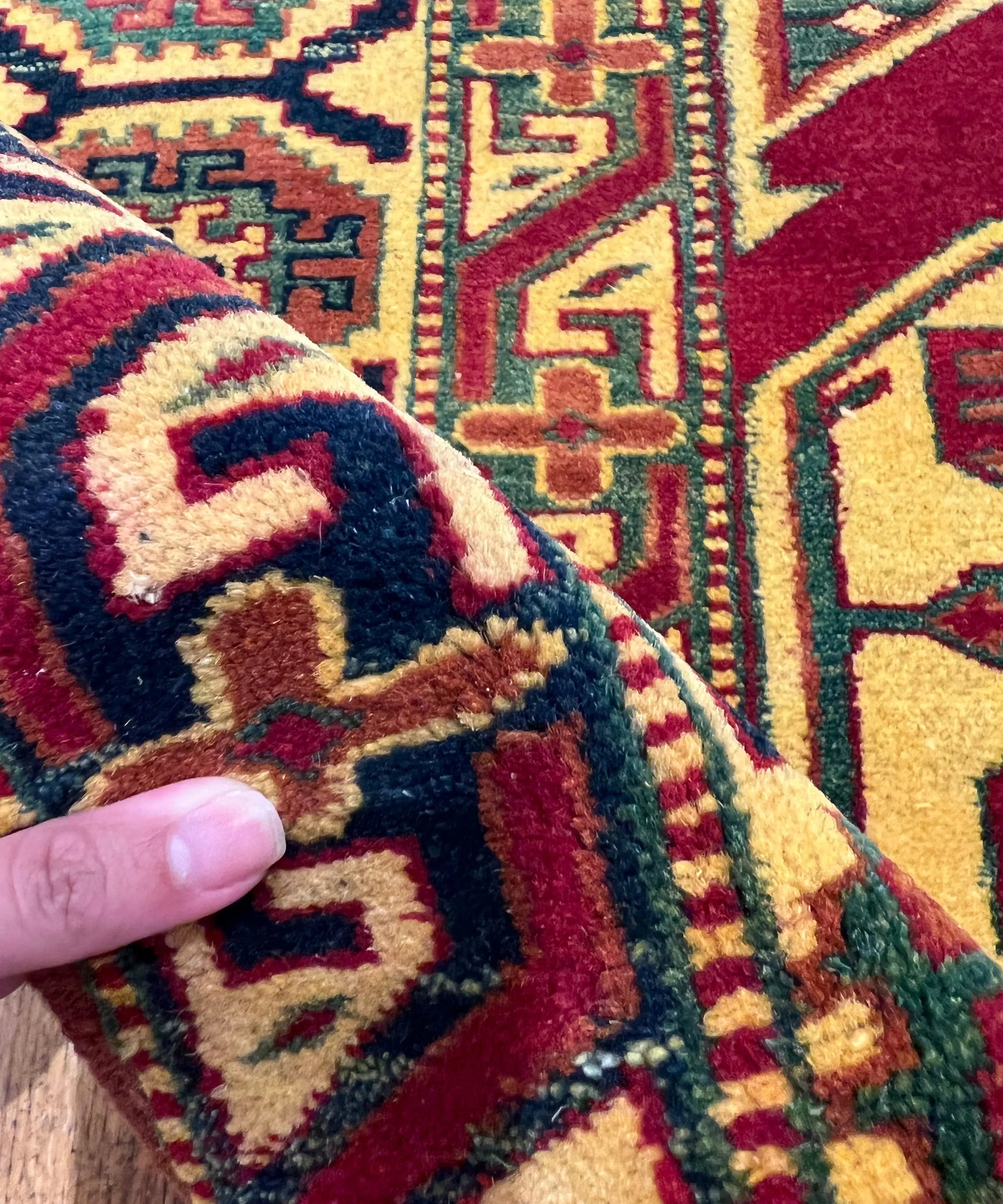 Hand holding Kazak rug edge with colorful geometric pattern and thick pile