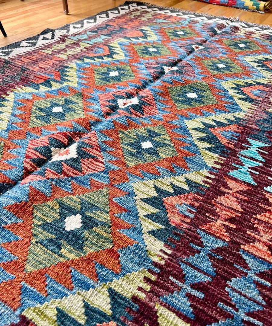Afghan kilim rug closeup with zigzag and diamond motifs in blue, orange, and teal