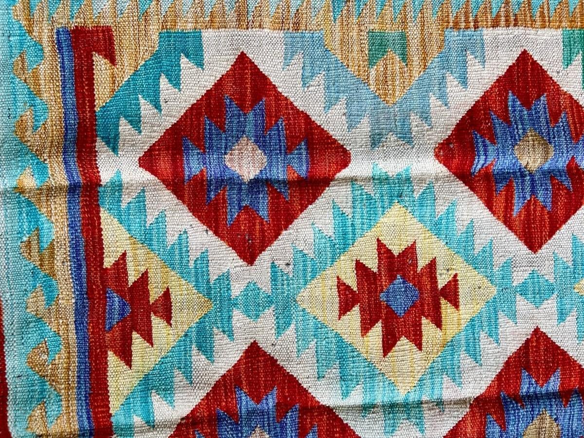 Kilim runner rug close-up with red diamond medallions on white and turquoise background