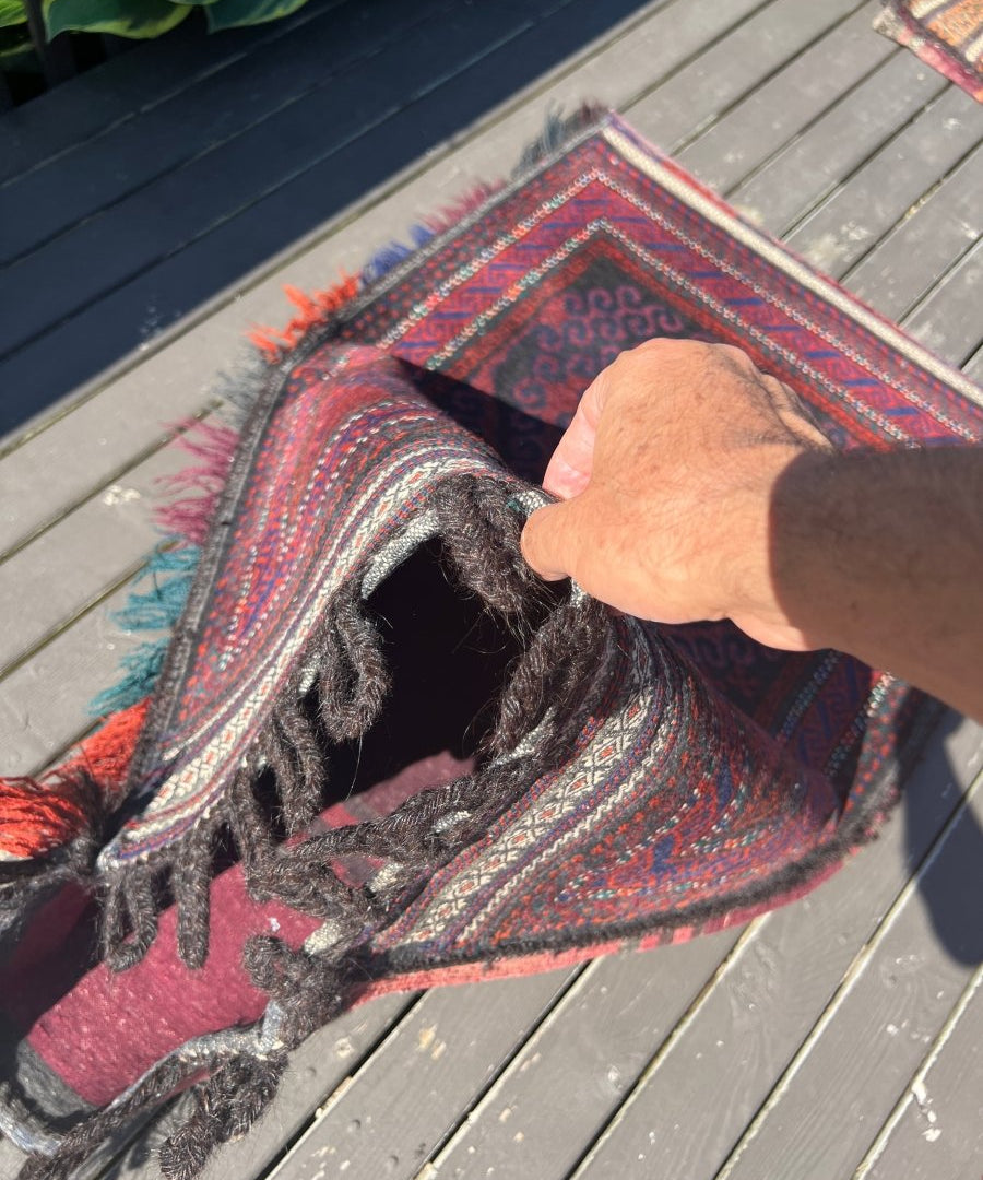 Antique saddlebag rug corner with fringe and patterned border in red, navy, and teal.