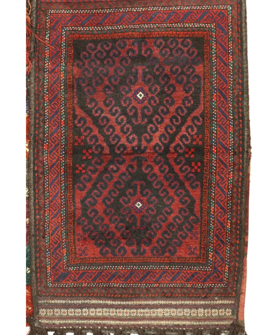 Antique Baluch saddlebag rug with red medallion pattern, navy border, and tassel fringe.