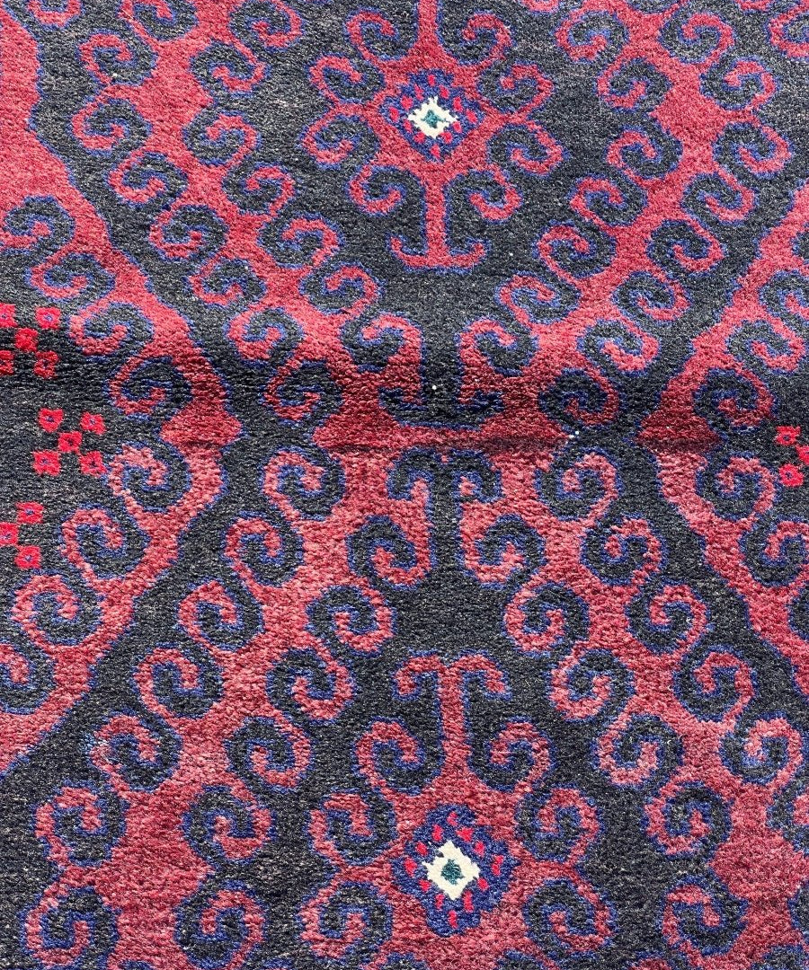 Close-up saddlebag rug showing red field with navy linked motifs and small teal rosette.