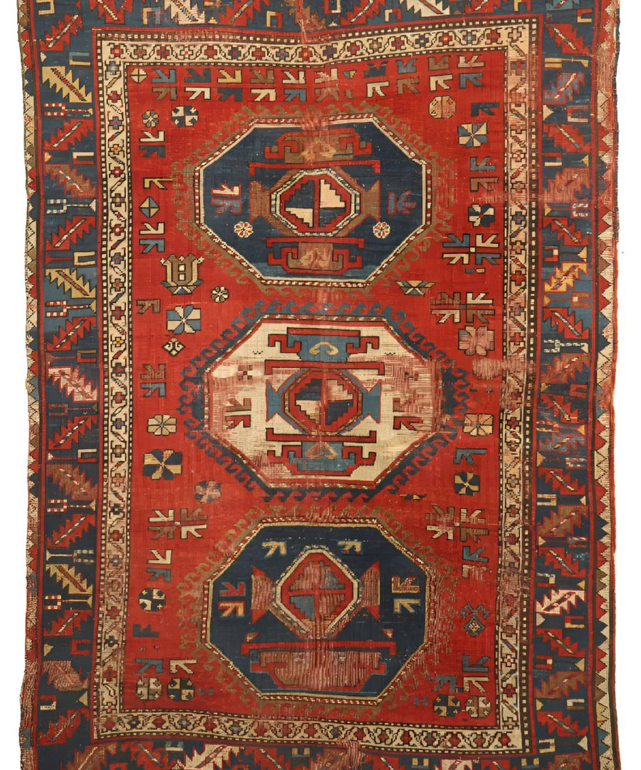 Antique red geometric wool rug with central medallions and detailed border pattern.