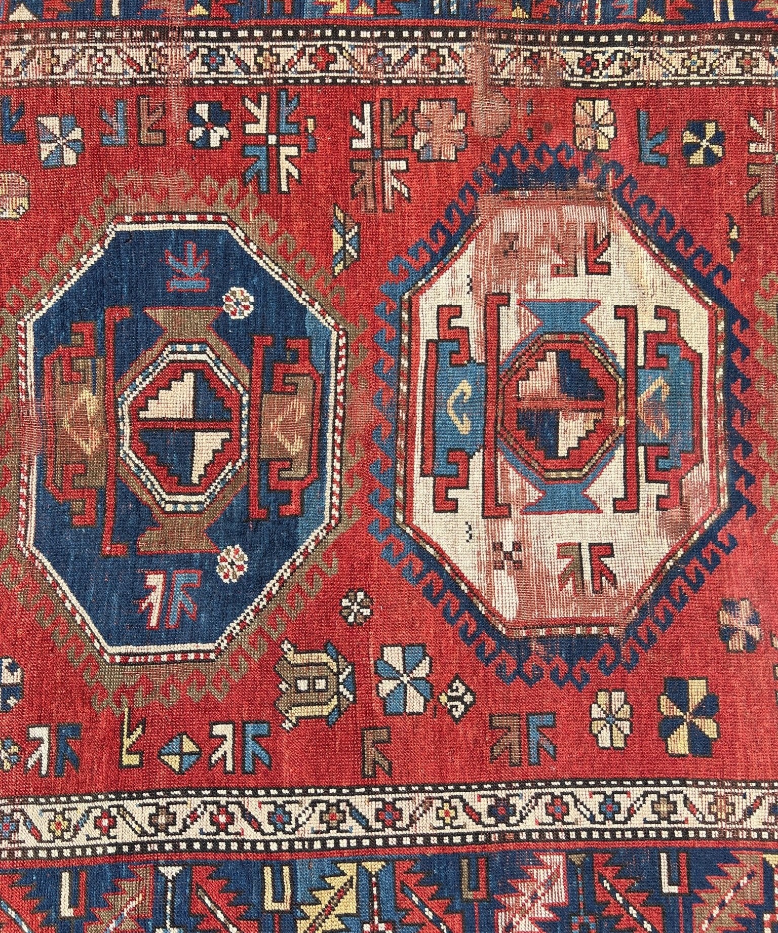 Antique red and blue geometric rug close-up with repeating motifs and medallion shapes.