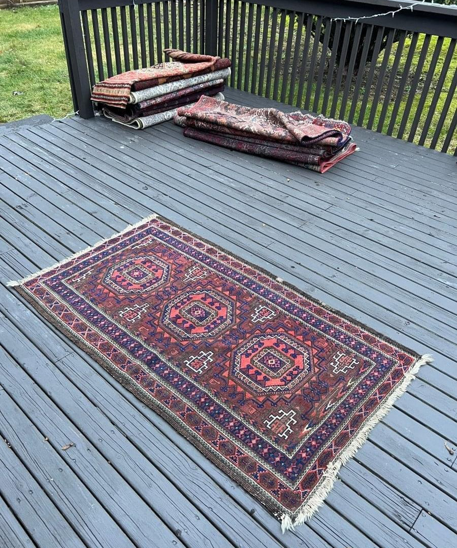 Persian Baluch rug laid on deck boards, red navy and cream geometric motifs, fringe ends