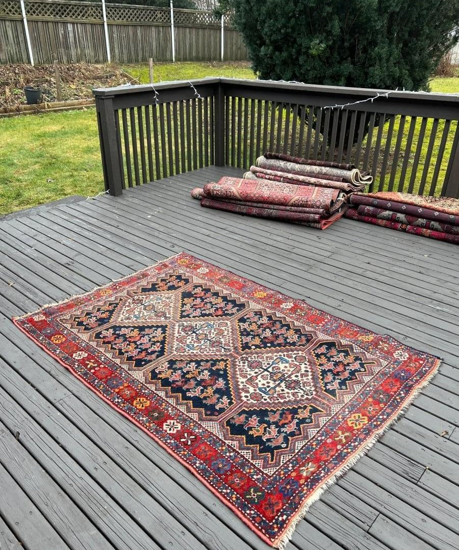 Antique Persian Khamseh rug with red border and navy field, folded for display