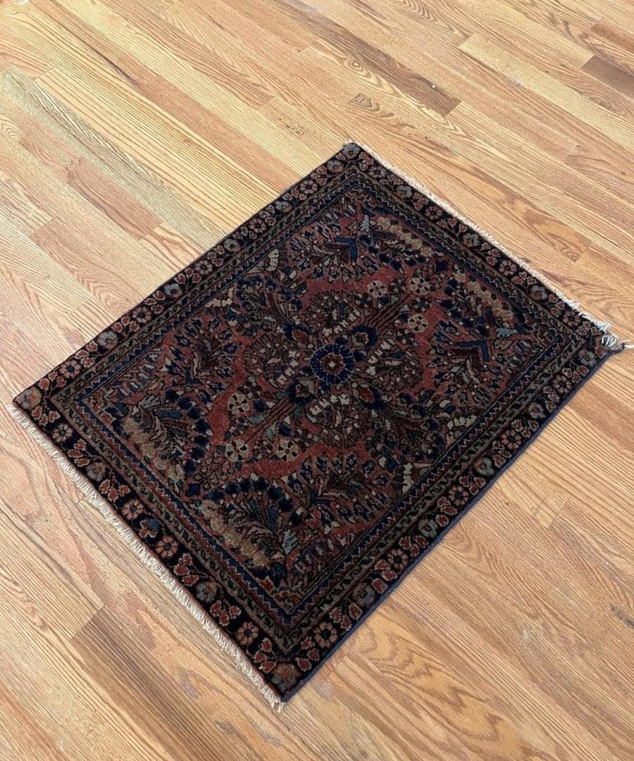 Antique Persian Sarouk rug angled on floor, navy border and red-rust medallion with motifs