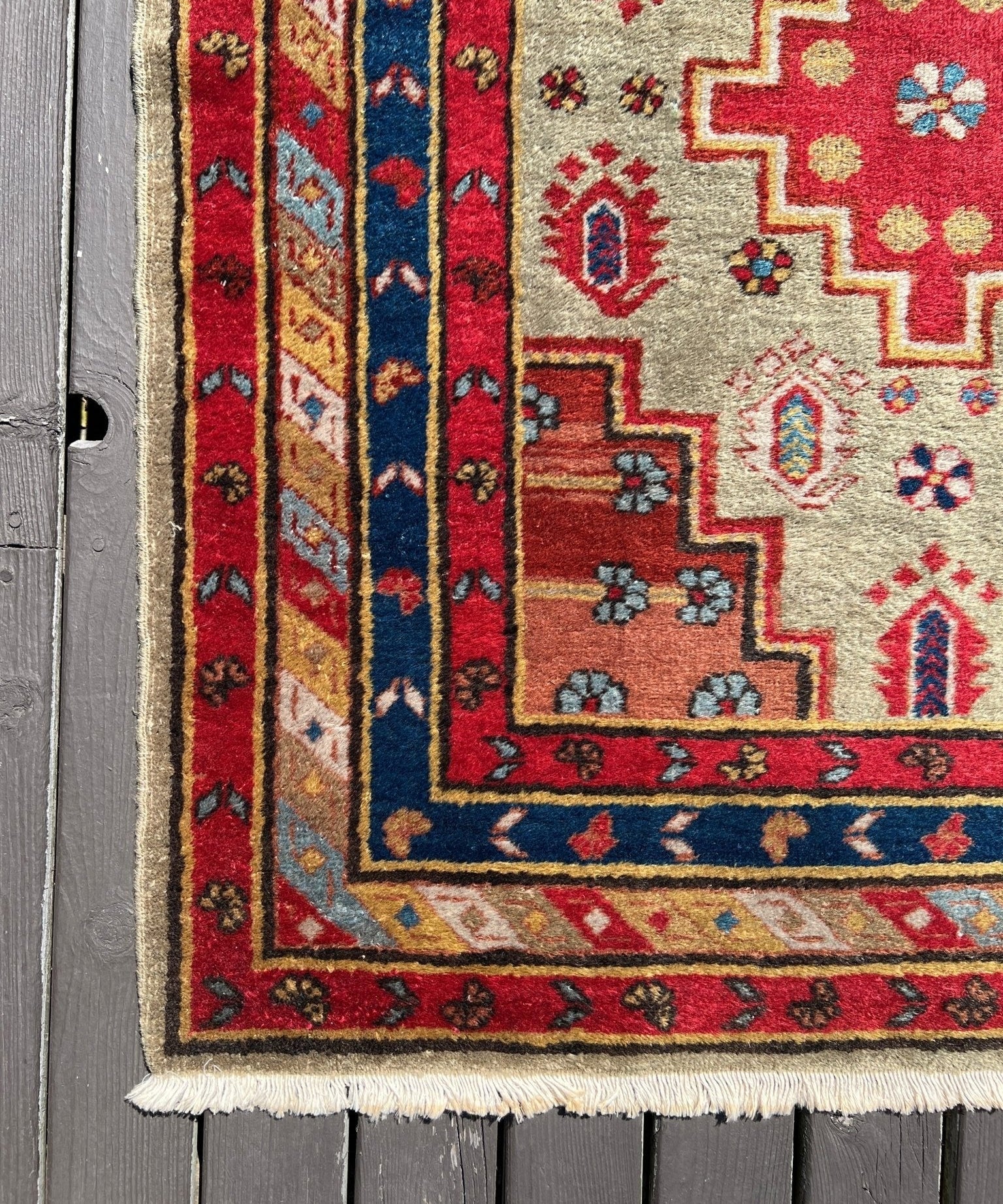 Rug corner detail with red and blue vertical stripes, cream field, and fringe border
