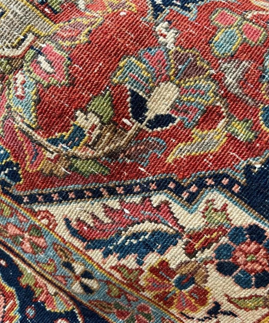 Close-up of antique rug weave with red field and multicolor floral motifs, patterned border