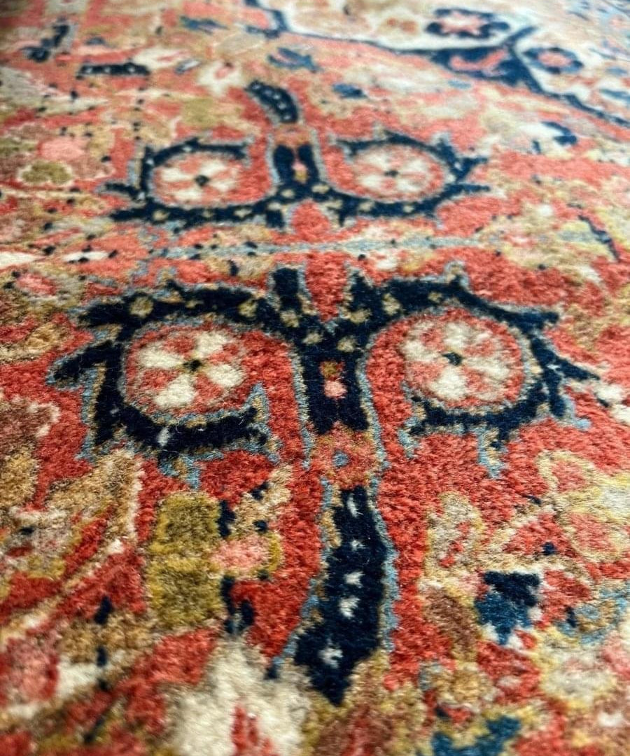 Close-up of antique rug pattern: red background with cream, navy, and teal floral details