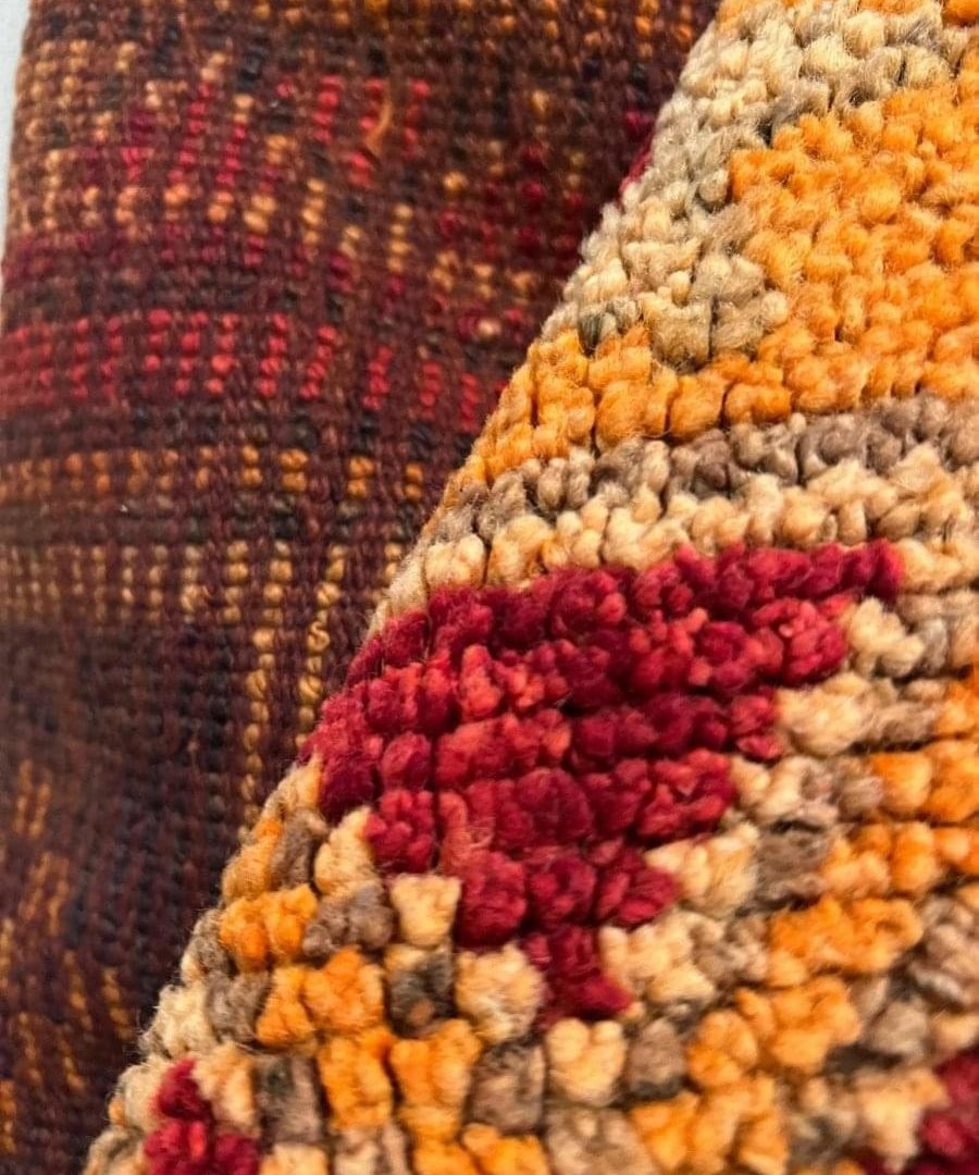 Woven rug corner with orange, red, and beige tufted texture and fringe