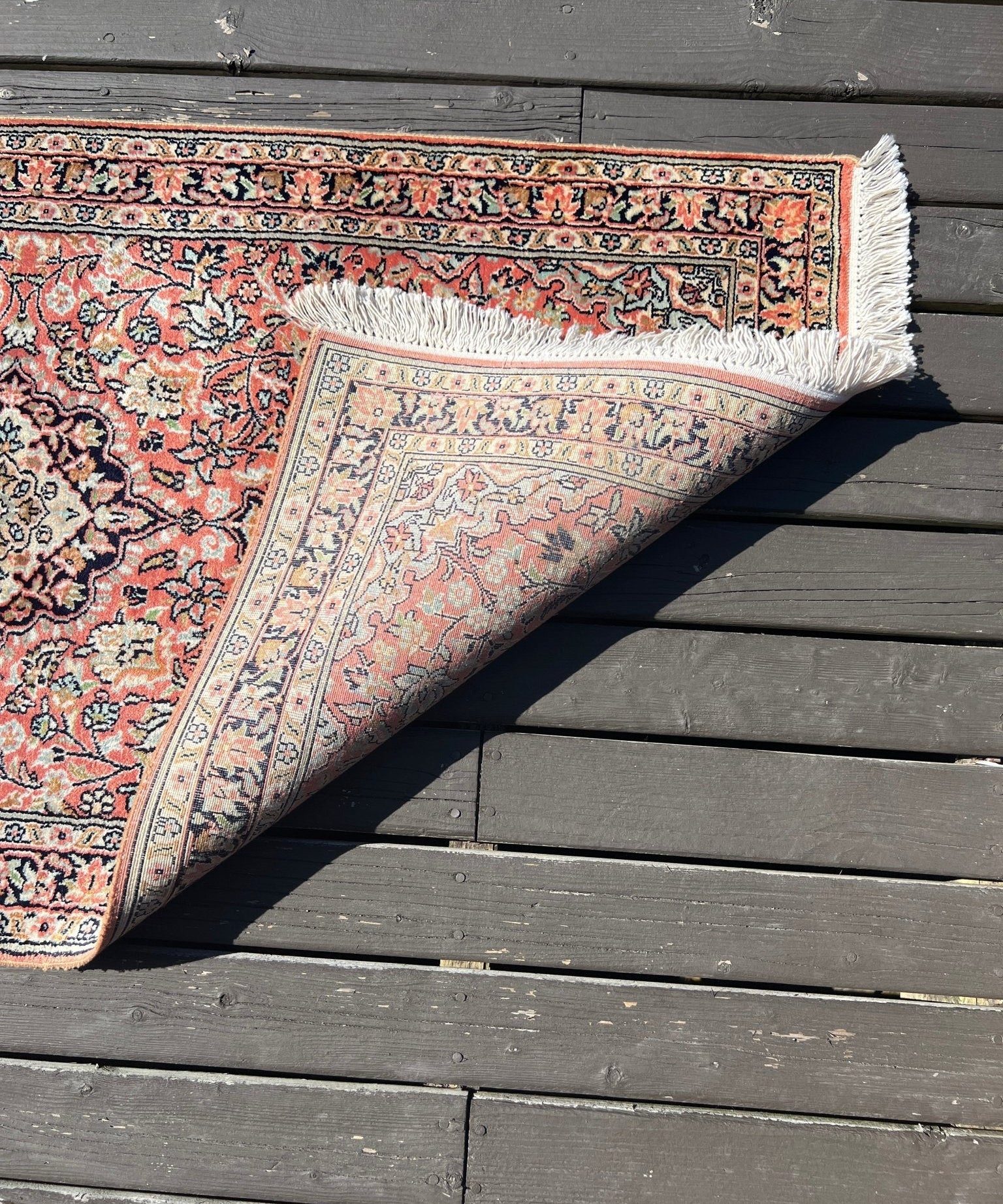 Corner view of a red and cream area rug with ornate border and tassel fringe