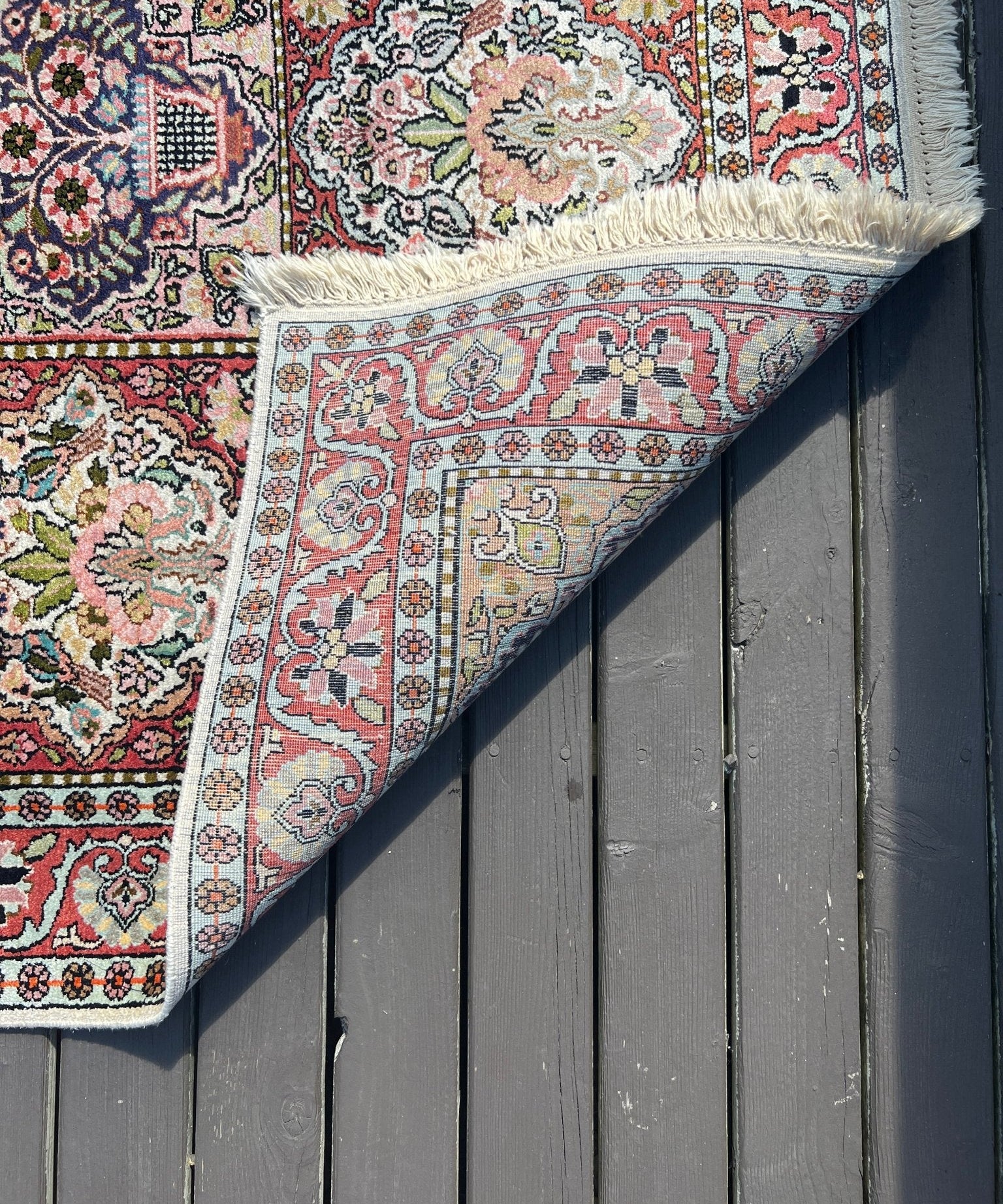 Red and cream rug corner with ornate multicolor border motifs and short fringe