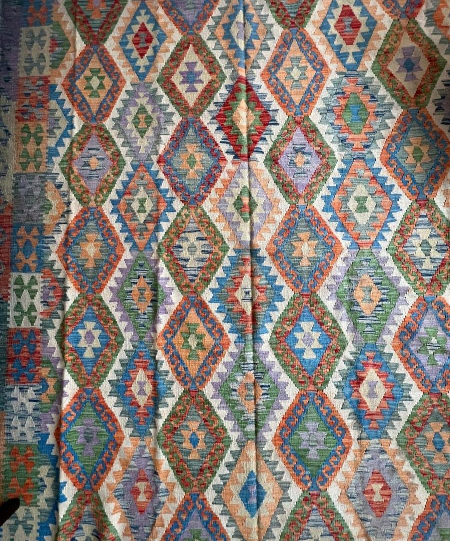 Geometric kilim rug with repeating diamond shapes in blue, red, green, and cream tones.