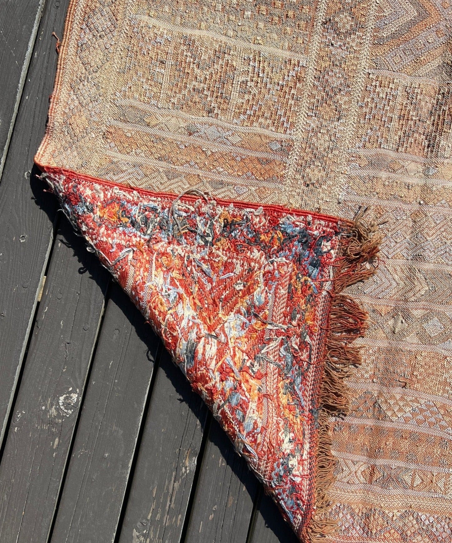 Moroccan woven rug corner, multicolor maroon and orange motifs with fringed edge