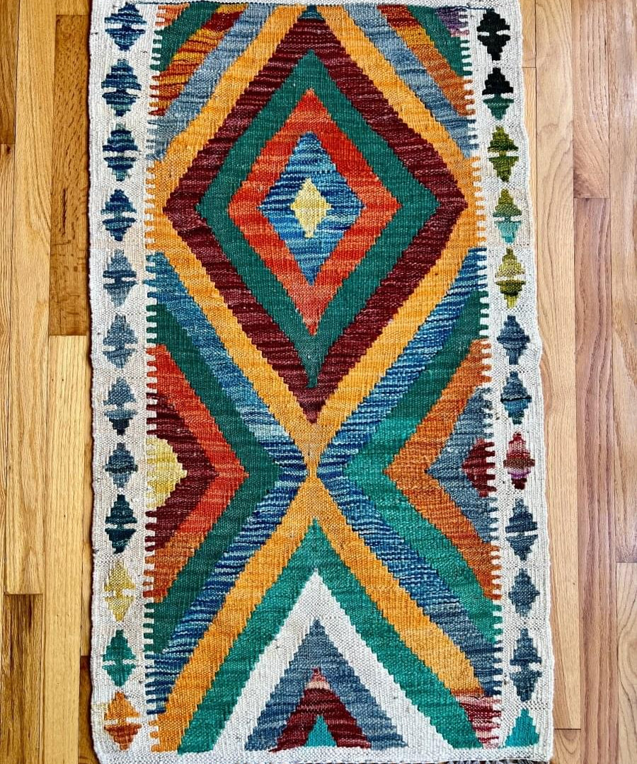 Kilim rug with geometric diamond chevrons in blue, green, red, and fringe edges.