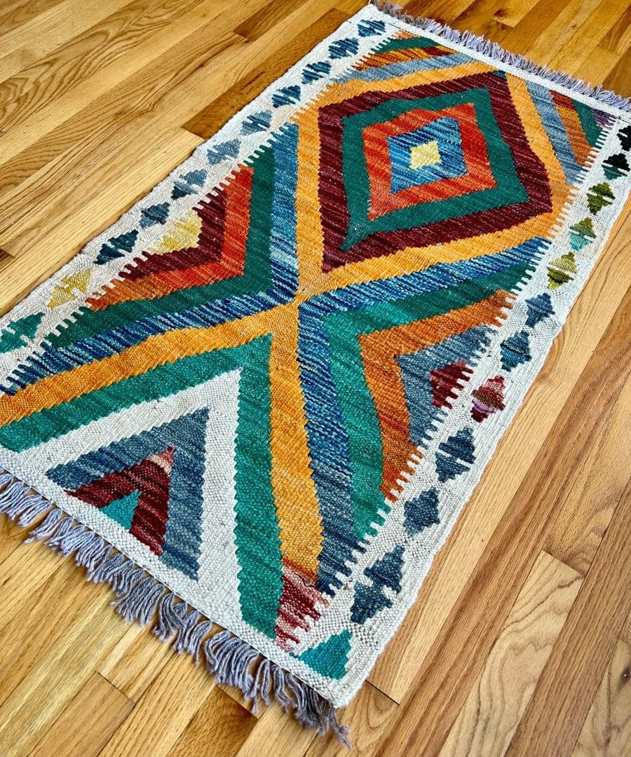 Geometric kilim rug with multicolor chevron pattern and fringed border, angled on floor.