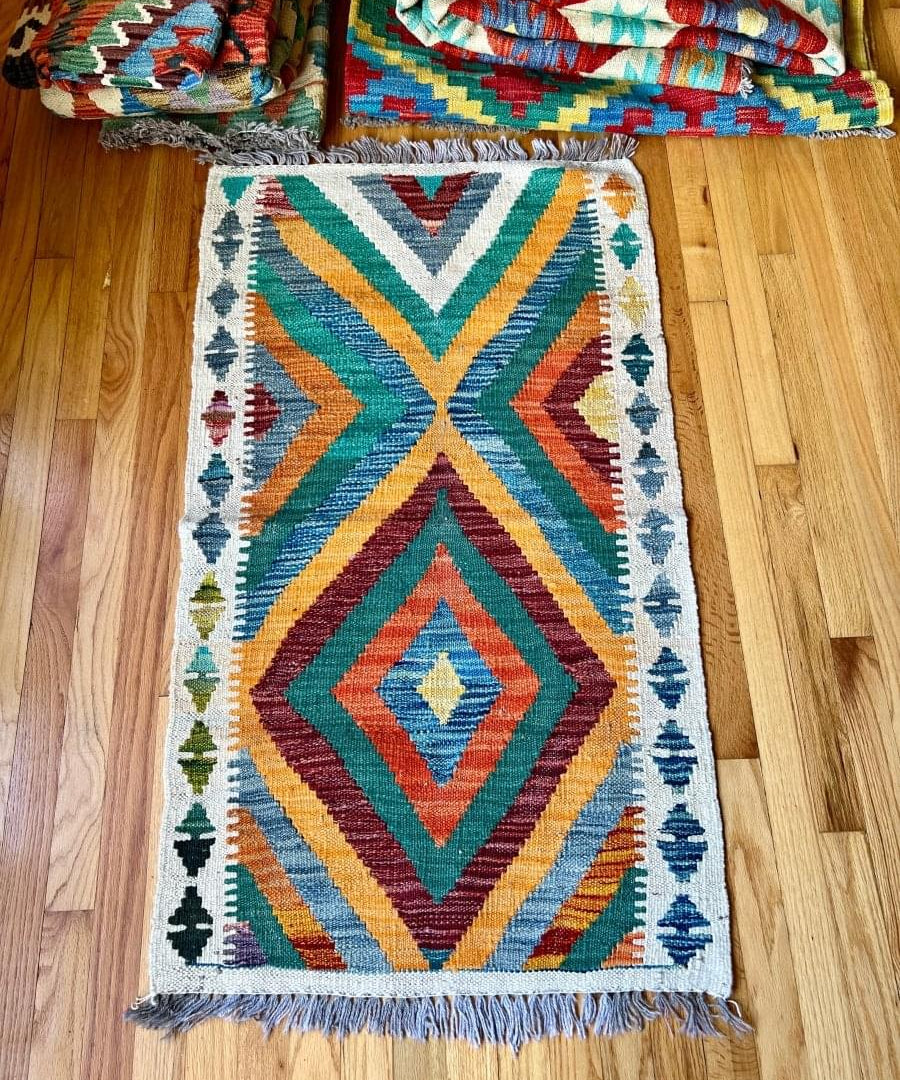 Small kilim rug with central diamond and chevron stripes in teal, blue, red; fringed.