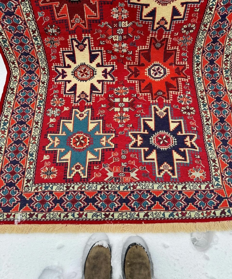 Red, blue, and cream geometric rug panel with borders; two brown shoes on it