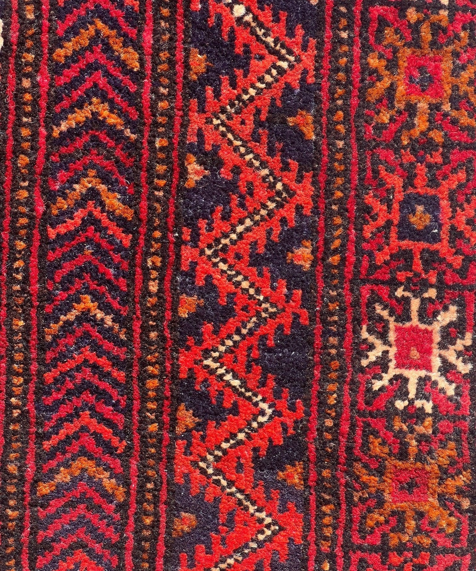 Baluch rug close-up featuring red-and-navy zigzag stripes and small cream pattern accents