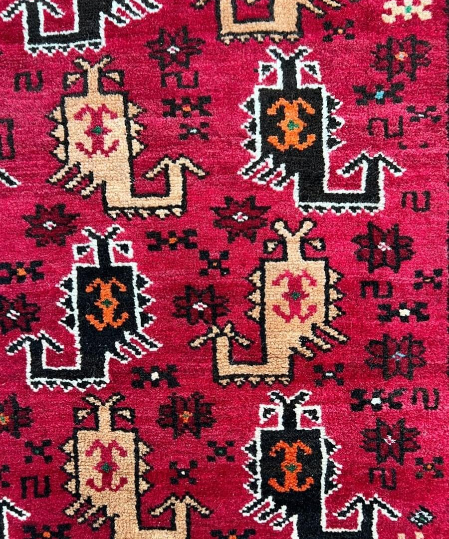 Baluch rug close-up: red background with cream, black, and orange geometric motifs