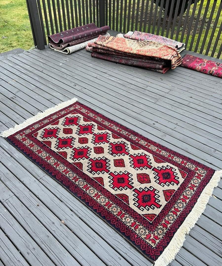 Persian Baluch rug on deck boards, ivory ground with red and dark blue medallions, fringed