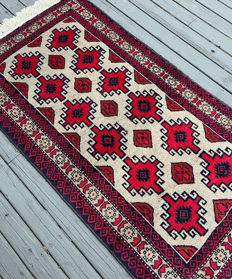 Persian Baluch rug at angle, ivory field with red and dark blue geometric border and motifs