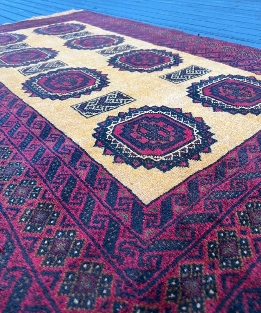 Persian Baluch rug close view: cream center with burgundy diamond medallions and blue accents.