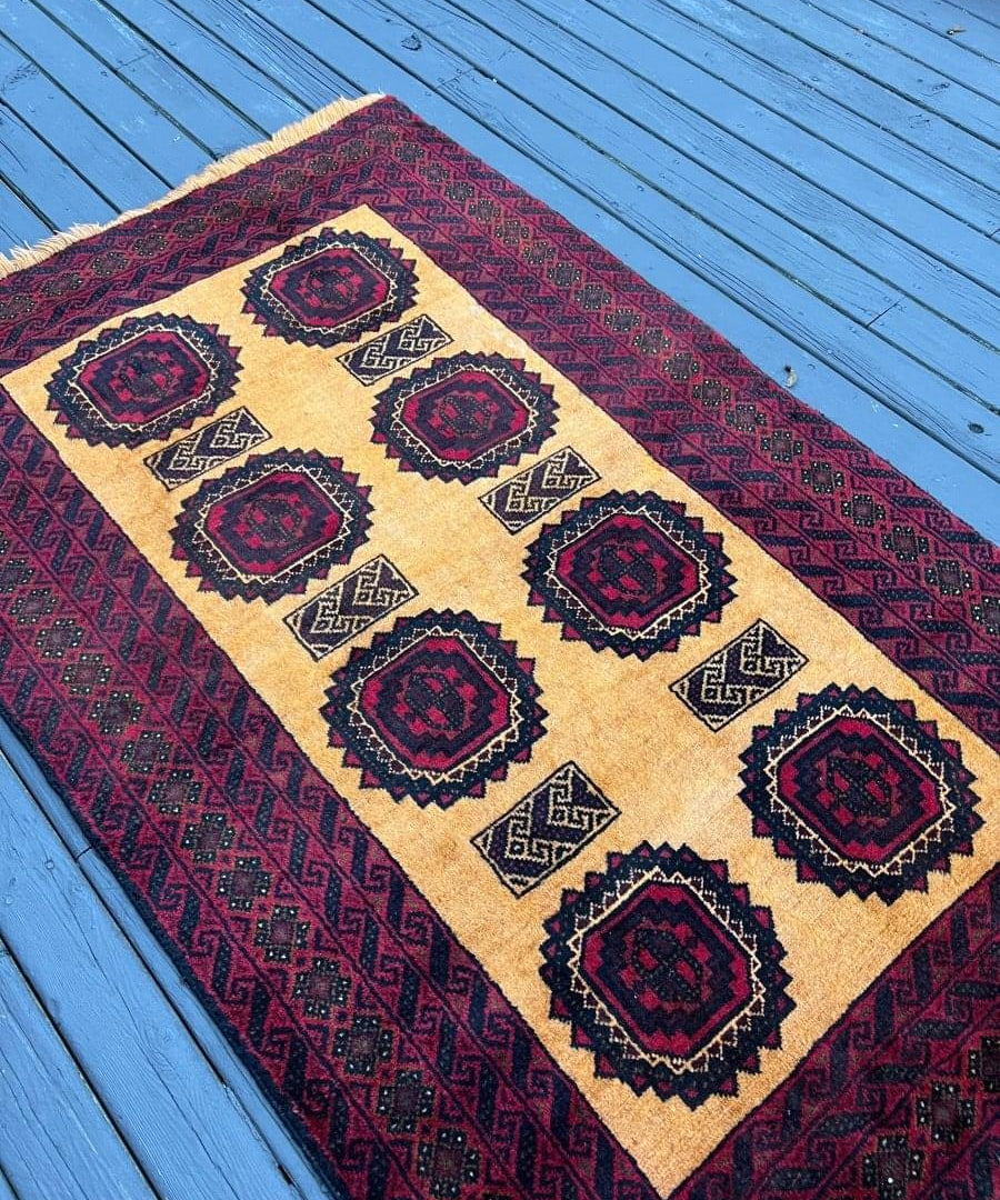 Persian Baluch rug: cream field with dark blue and burgundy diamond medallion pattern.