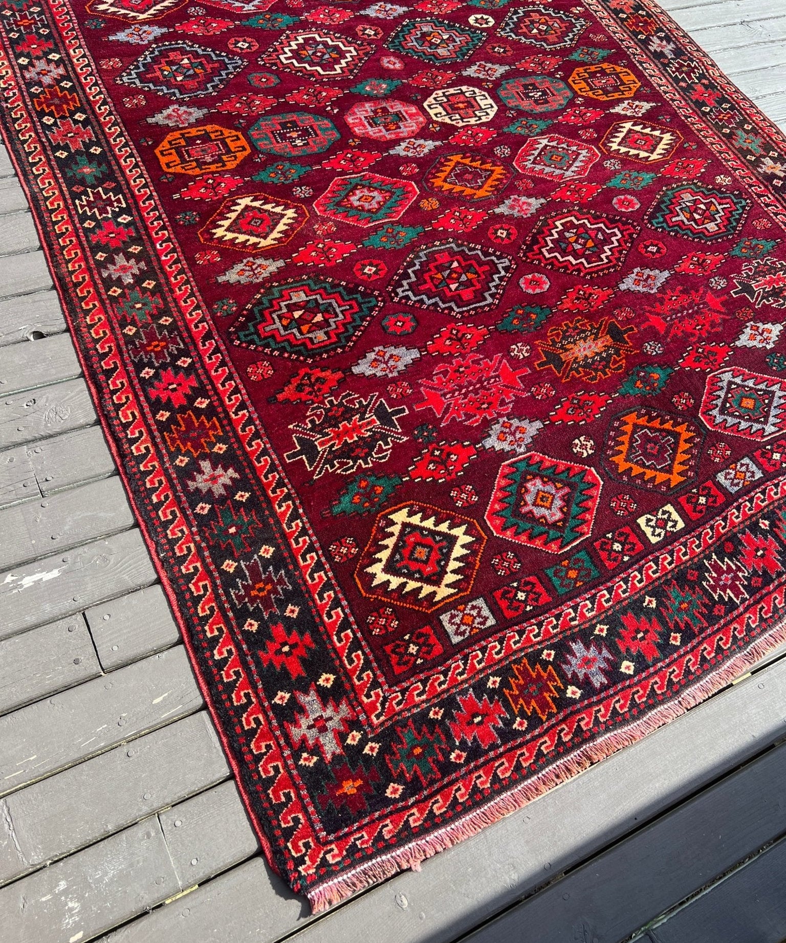 Persian Quchan rug with dark red field, multicolor geometric motifs, and border stripes