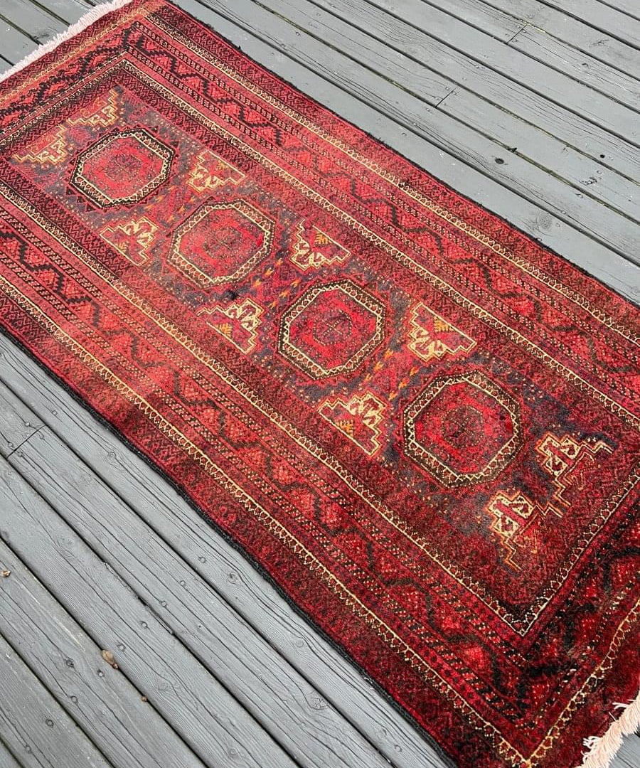 Red Persian Baluch rug runner with repeating diamond and medallion pattern, short fringe.