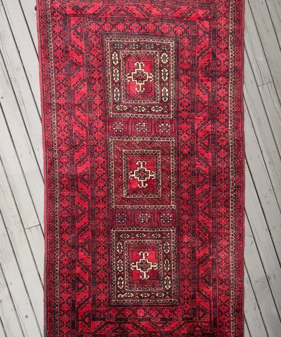 Red Persian Baluch rug with stacked medallion motifs and dark geometric border