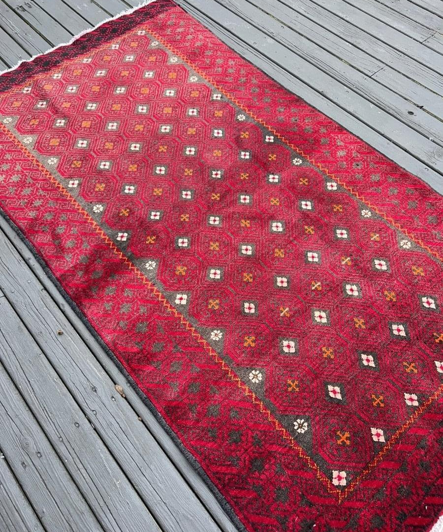 Persian Baluch-style rug with red ground, stepped border, and small motif squares