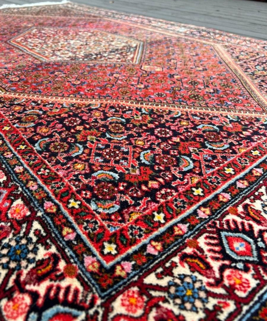 Red Persian-style bidjar rug corner close-up with navy, cream, and multicolor details.