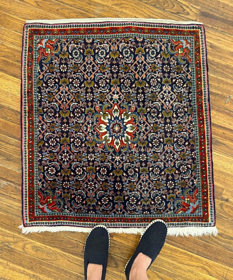 Persian Bijar rug with navy floral pattern, red border, and cream fringe edges