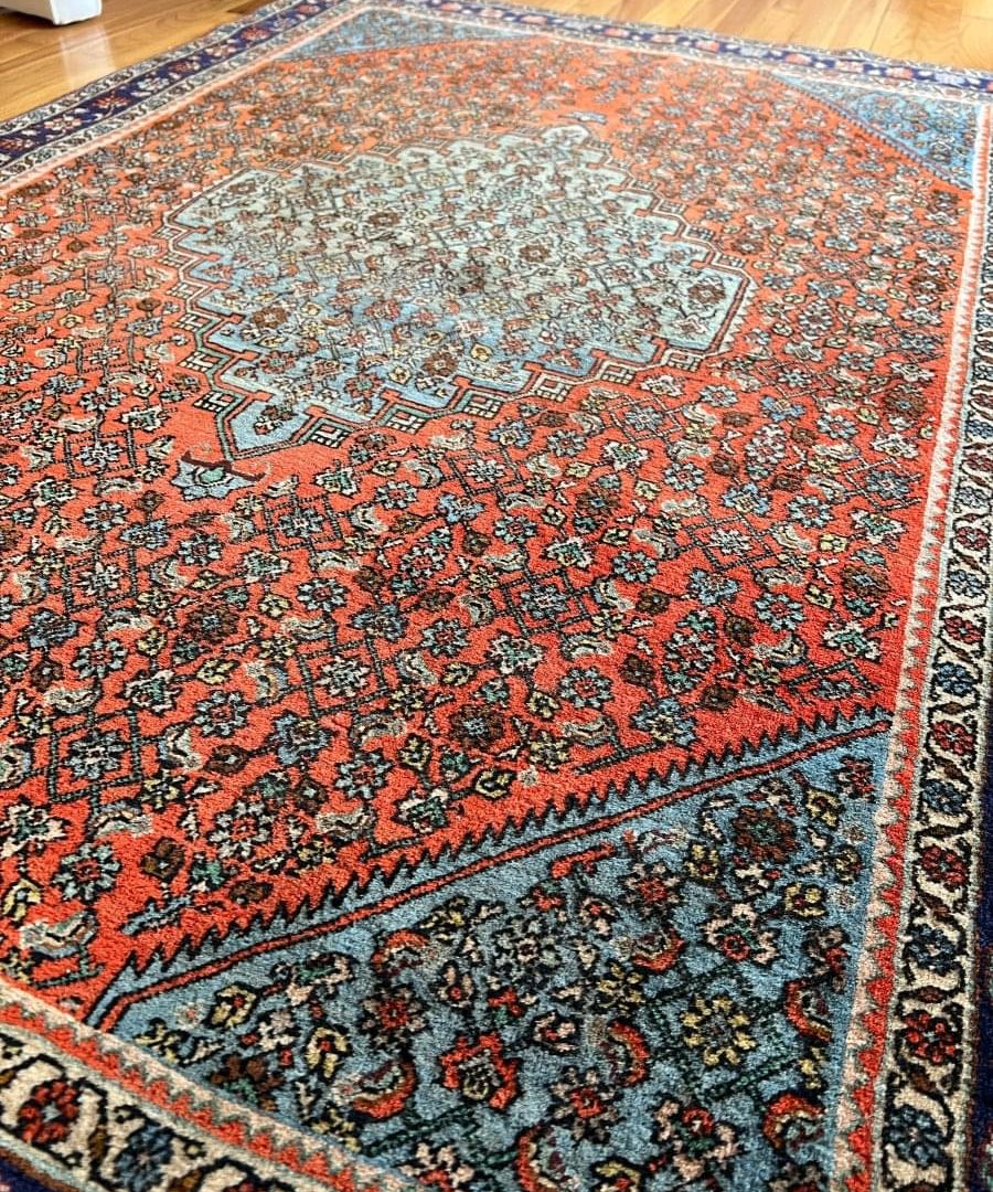 Persian Bijar rug with rust-orange design, light medallion center, and navy corner border
