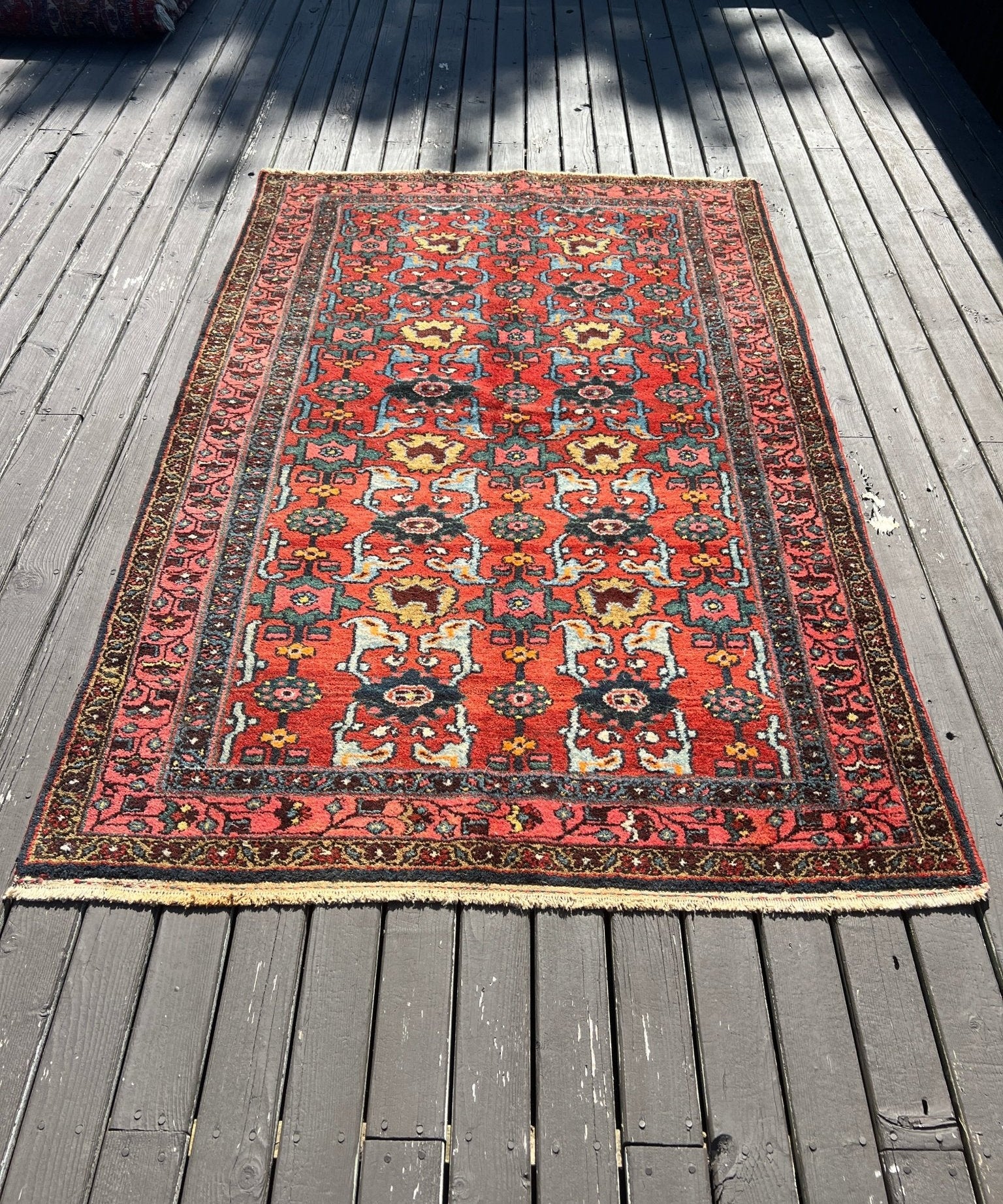 Red rug with central medallion and geometric motifs, Persian Hamadan style on deck boards