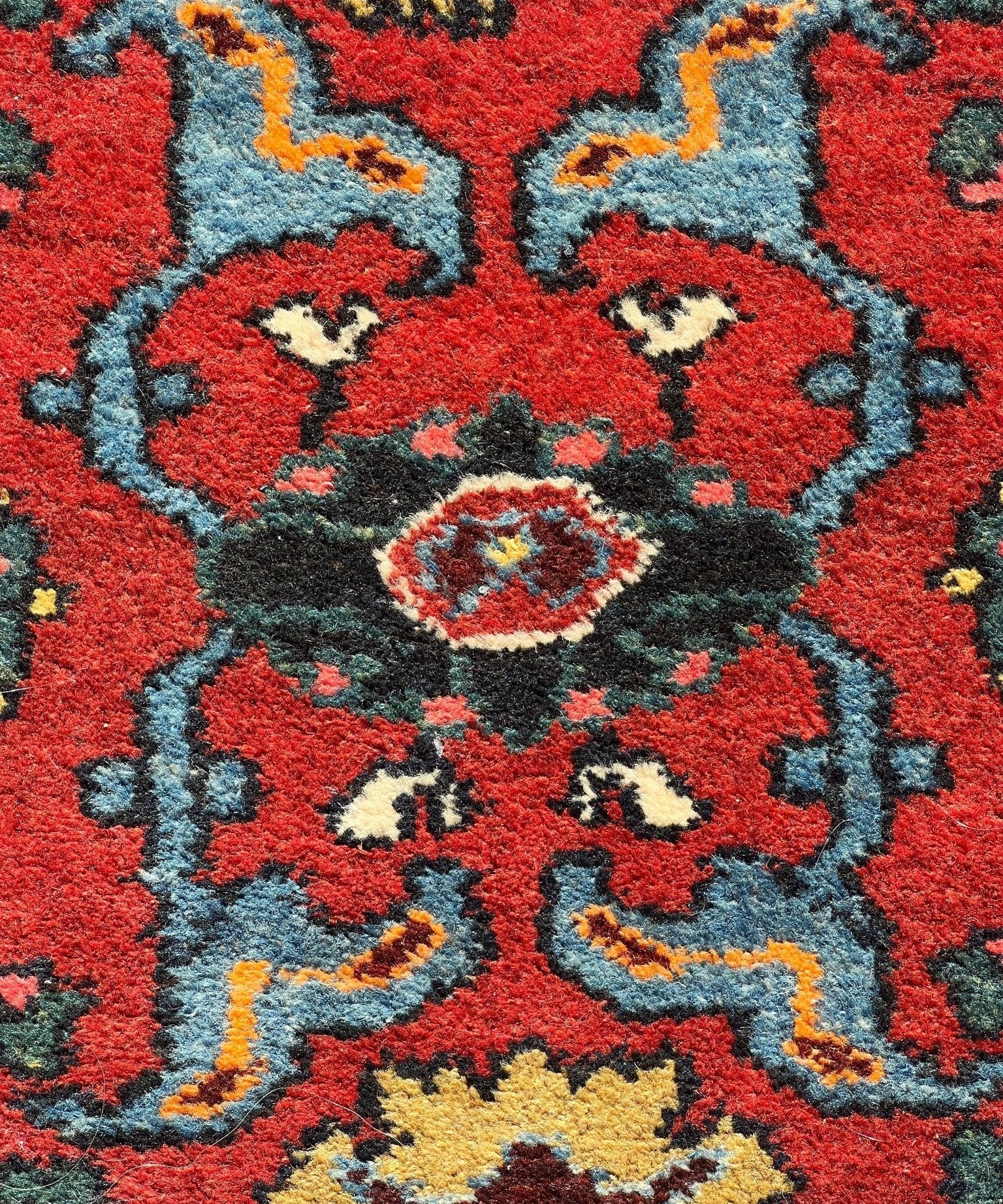 Red rug close-up with teal and blue scroll motifs and small medallion details