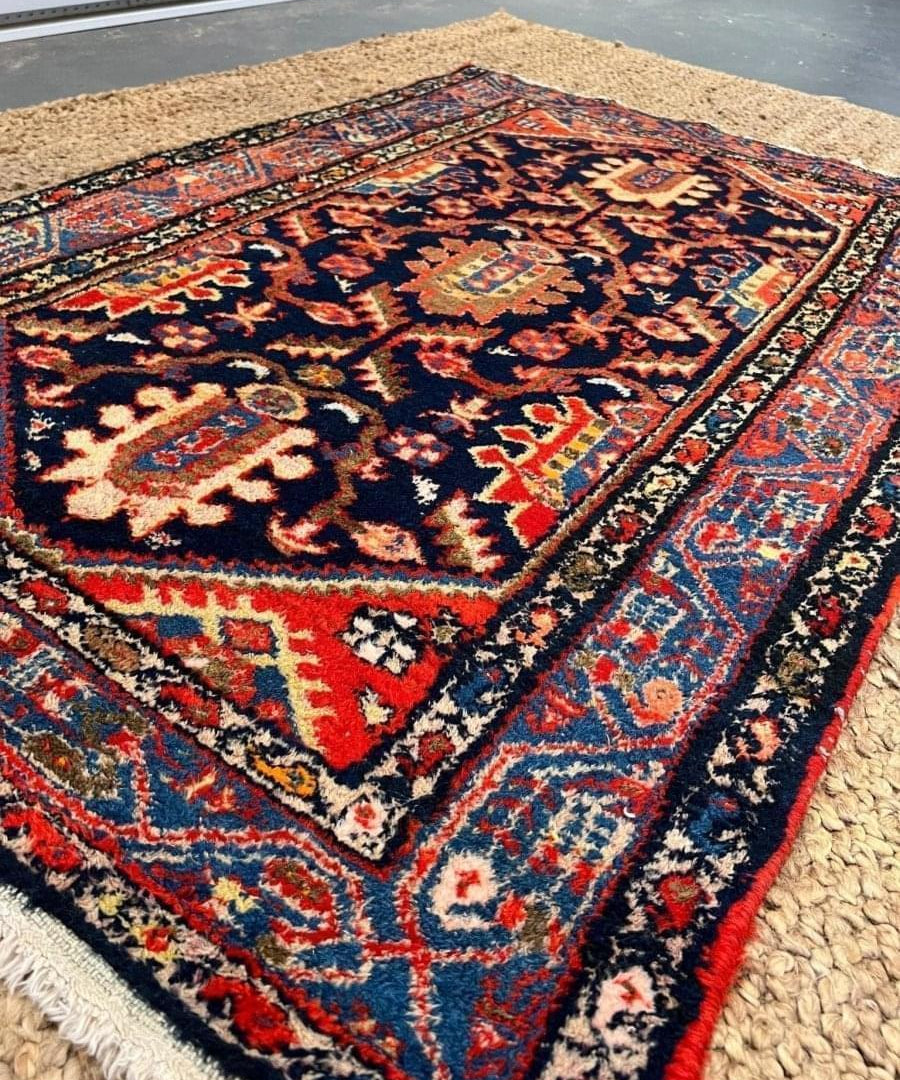 Persian Hamadan rug angled view, navy center with red, blue, and beige border details