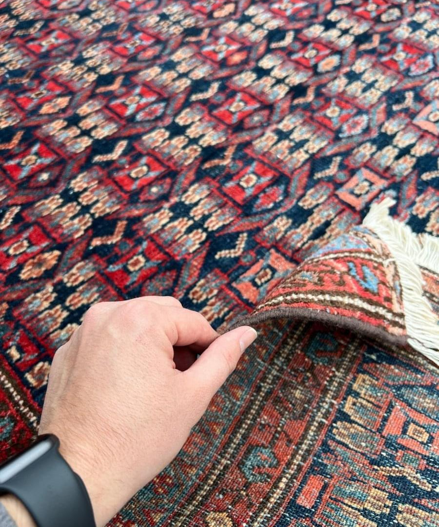 Persian Hamadan rug texture detail, hand holding corner with blue field and red diamond motifs