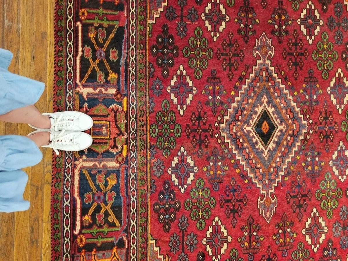 Red rug side border with geometric motifs beside white sneakers on wood floor