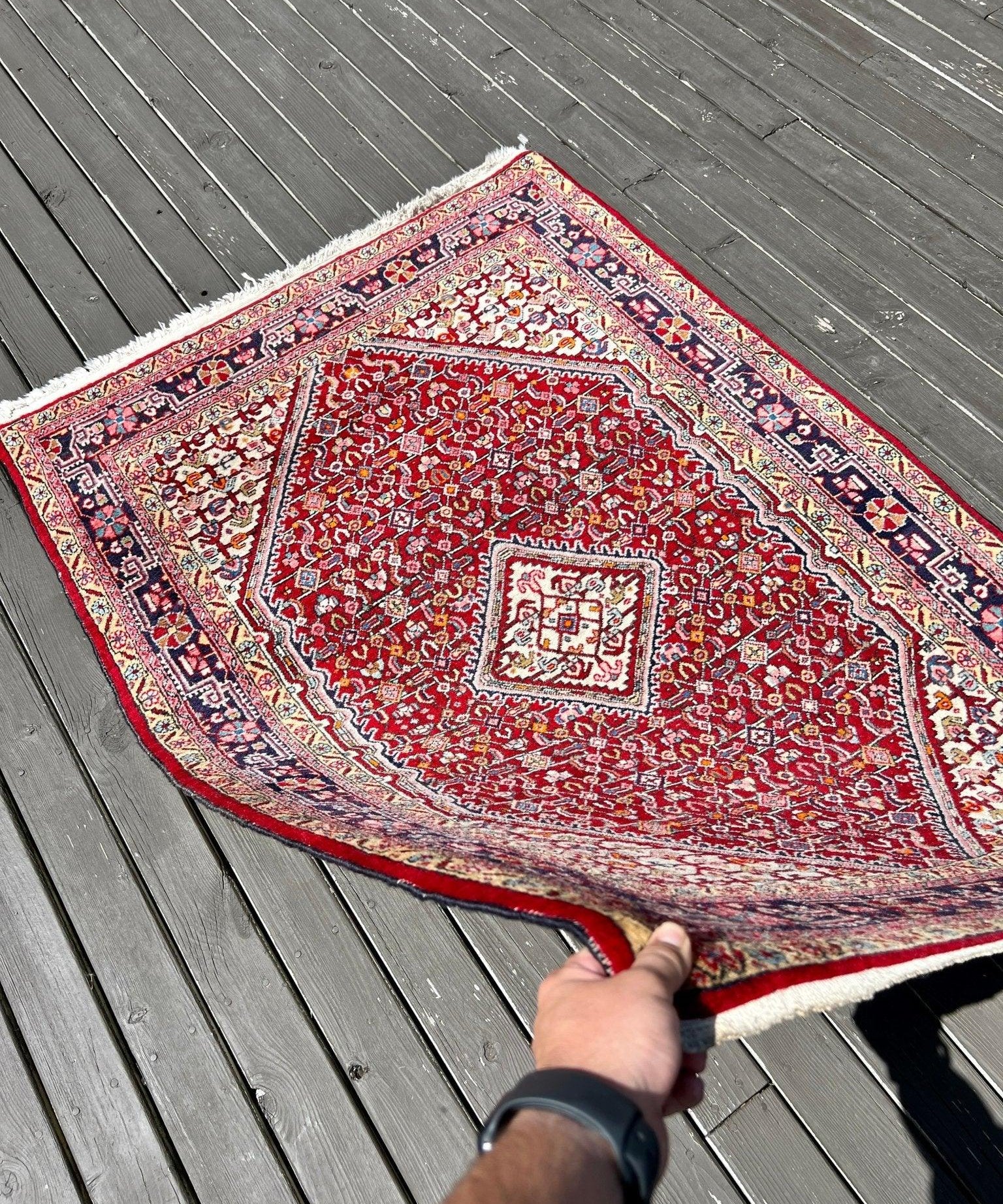 Persian Jozan rug corner held; red floral medallion pattern with multicolor border and fringe.
