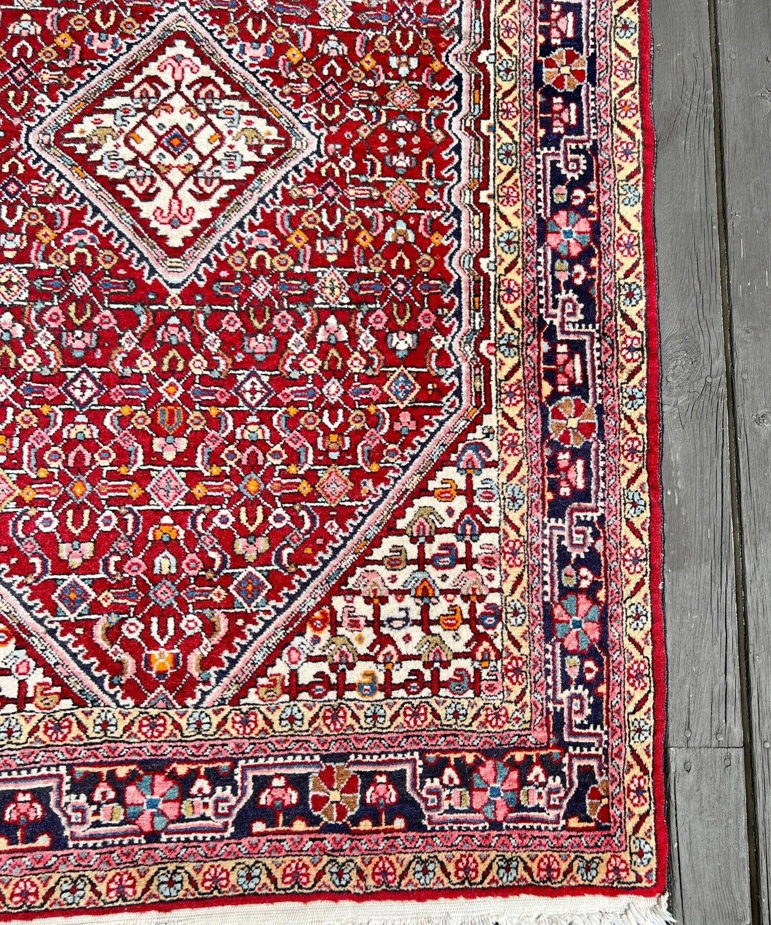 Persian Jozan rug close-up: red field, ornate border trim, and white fringe along the edge.