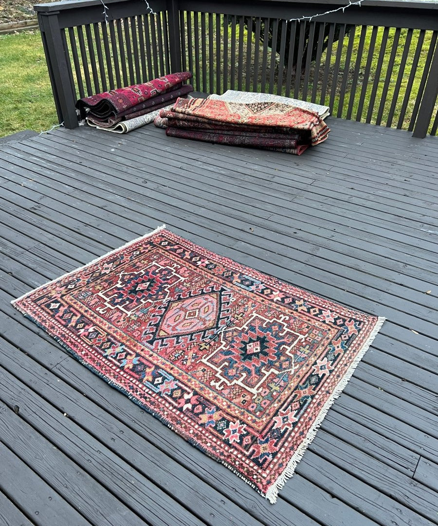 Persian Karaja rug laid flat, maroon and teal geometric pattern with fringe.